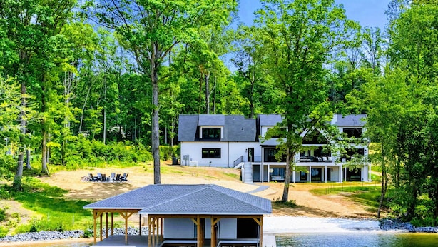 A lakeside cabin with a dock, a covered seating area, and a modern house in the background. - Lakefront Lake Anna, Beach, Dock, Deck Vie (Bumpass)