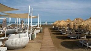 A beachside hotel with thatched umbrellas, lounge chairs, and a wooden walkway leading to the ocean. - Sea Breeze Stylish Studio with Private Terrace (Nardaran)