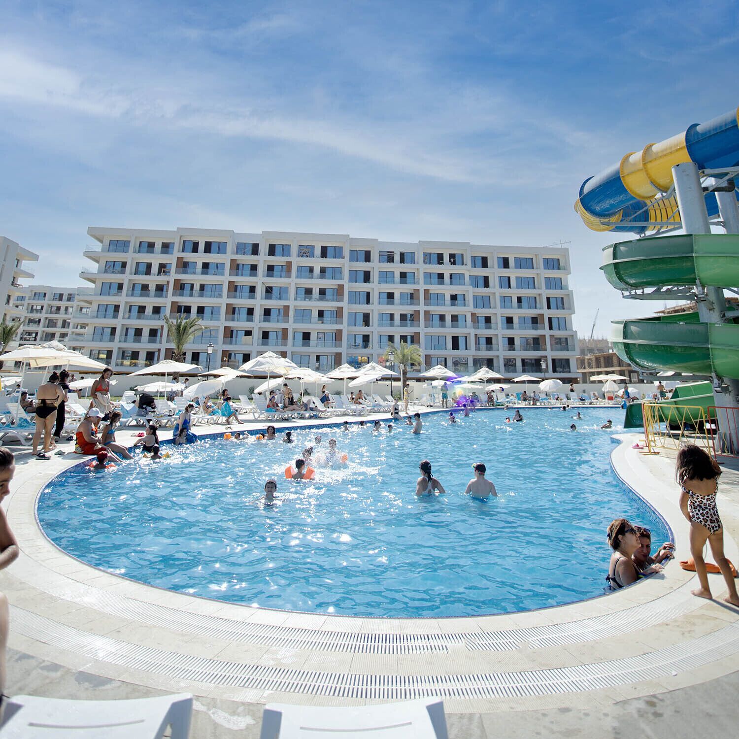 Une piscine entourée de chaises longues et de parasols, avec un toboggan aquatique en arrière-plan.