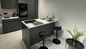 A modern kitchen with a central island, bar stools, and a small table with a vase. - Sea Breeze Stylish Studio with Private Terrace (Nardaran)