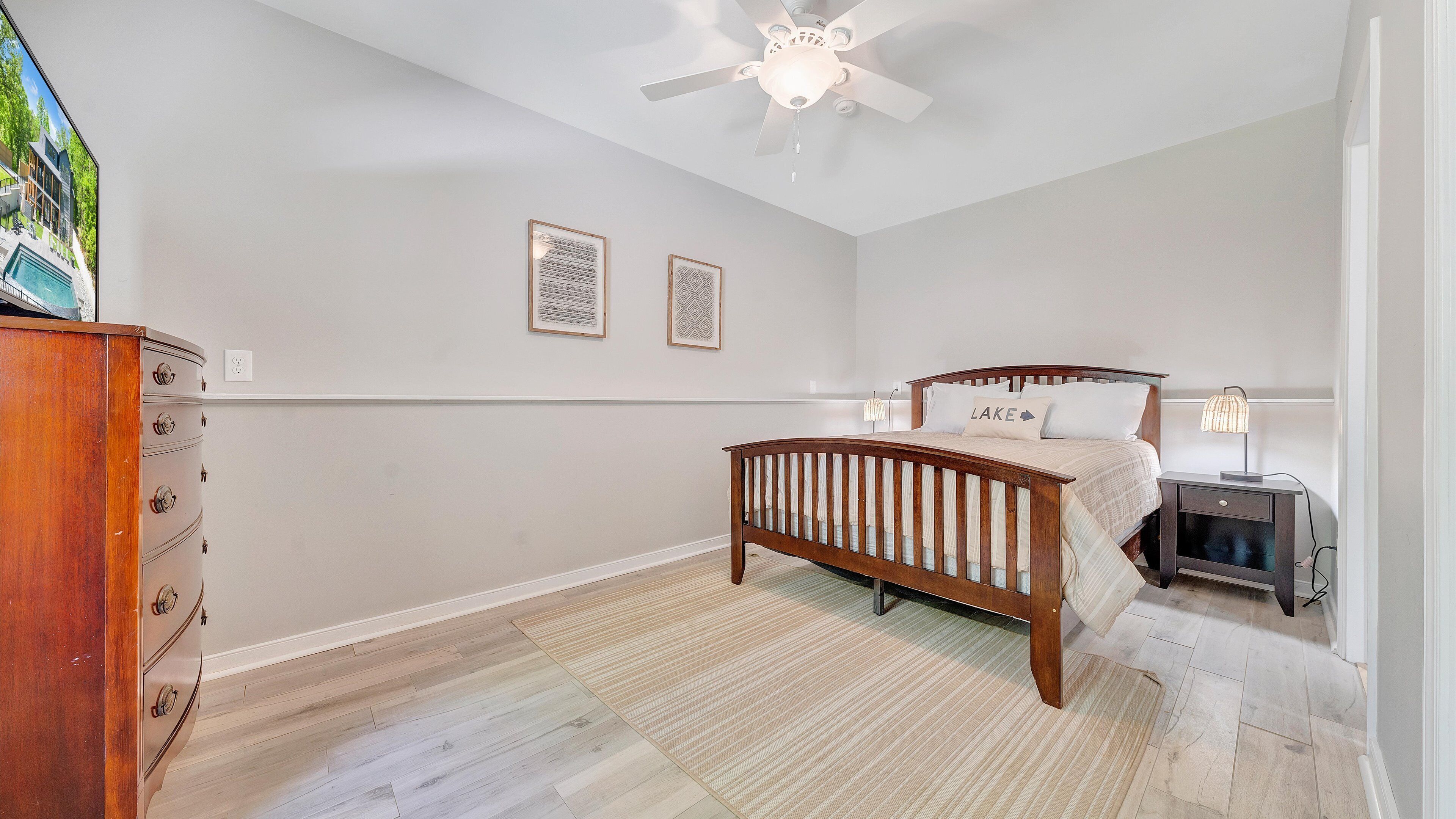 A bedroom with a wooden bed, a nightstand, a ceiling fan, and a dresser.