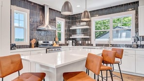 Una cocina moderna con una isla central, iluminación colgante y ventanas amplias.
