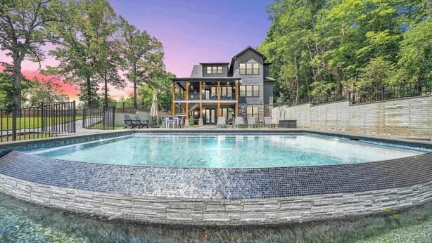 A swimming pool with a stone border, a two-story building with a balcony, and a stone wall.