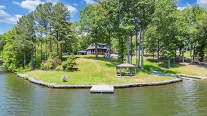 A lakeside property with a dock, a gazebo, and a large house surrounded by trees.