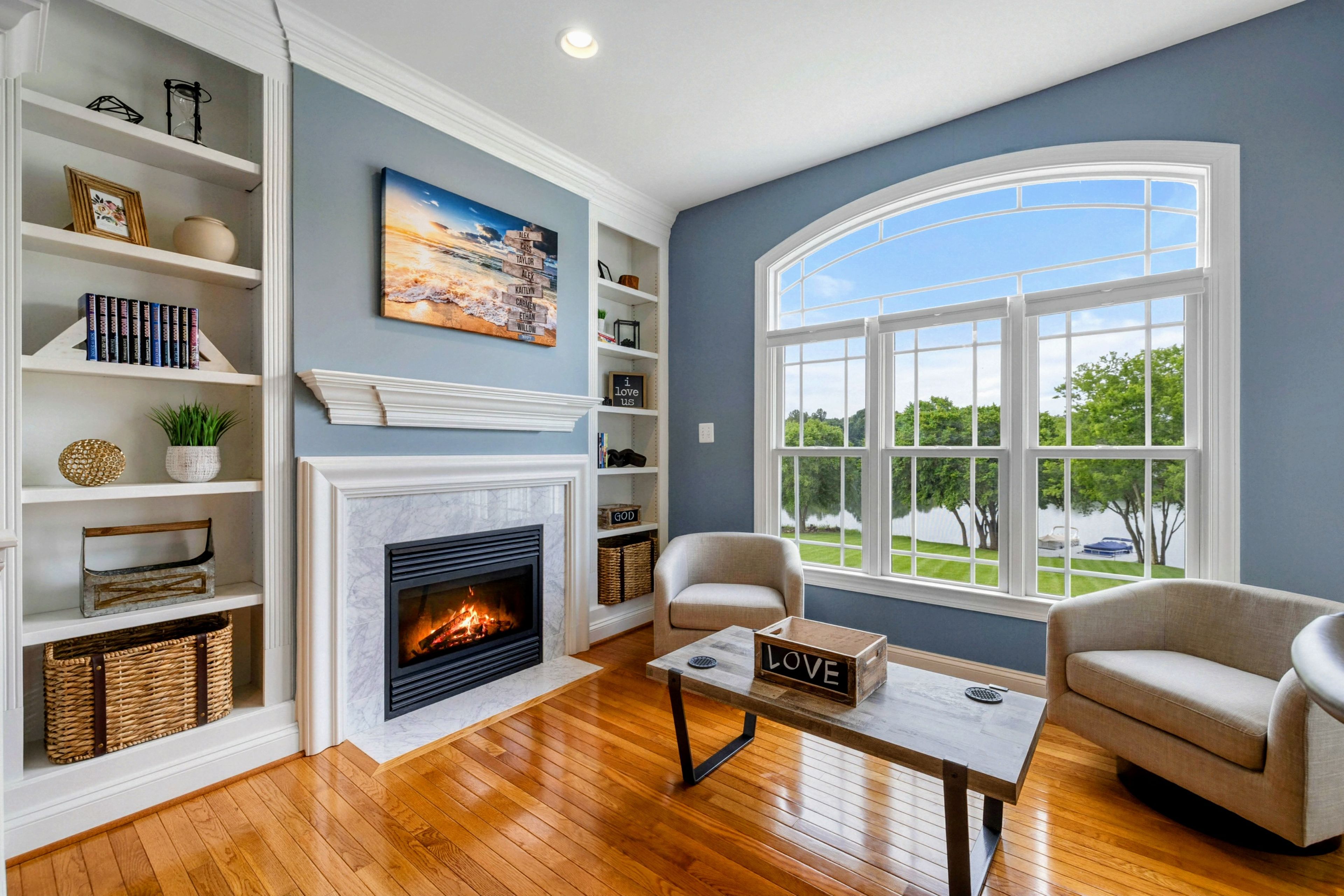 A living room with a fireplace, bookshelves, a coffee table, and a view of the outdoors.