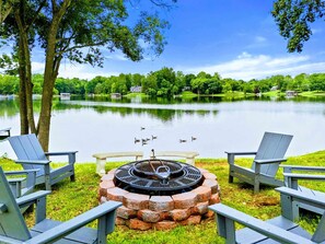 Une vue sur le lac, avec des fauteuils Adirondack, un foyer et une maison en arrière-plan.