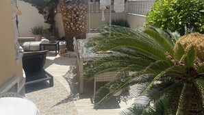 Un espace patio aménagé avec du mobilier d’extérieur, un parasol blanc et des plantes en pot.