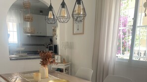 Un espace repas avec une table en bois, des chaises blanches et des lampes suspendues.