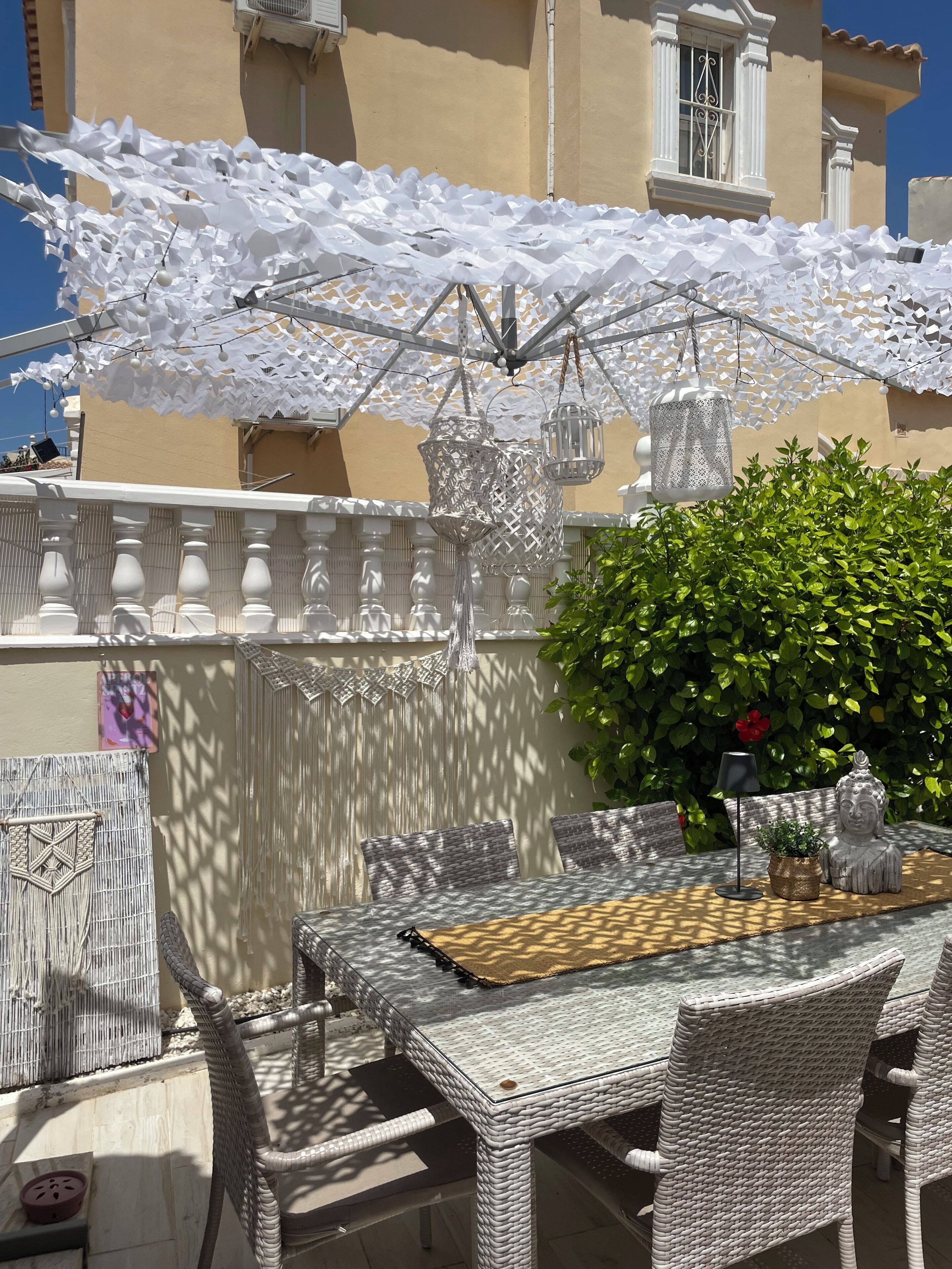 Een terras buiten met rieten meubels, witte parasols en decoratieve lantaarns.