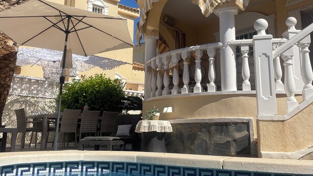 Un espace piscine avec une eau d’un bleu limpide, une balustrade blanche et un bâtiment beige doté d’un balcon.