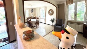 A dining area with a round table and chairs, a chandelier, and a view of the outdoors through large windows. - La maison aux oiseaux - Luberon (Oppède)
