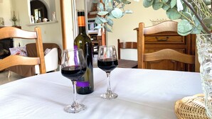 A dining table with two wine glasses and a bottle of wine, surrounded by wooden chairs and a vase with green foliage. - La maison aux oiseaux - Luberon (Oppède)