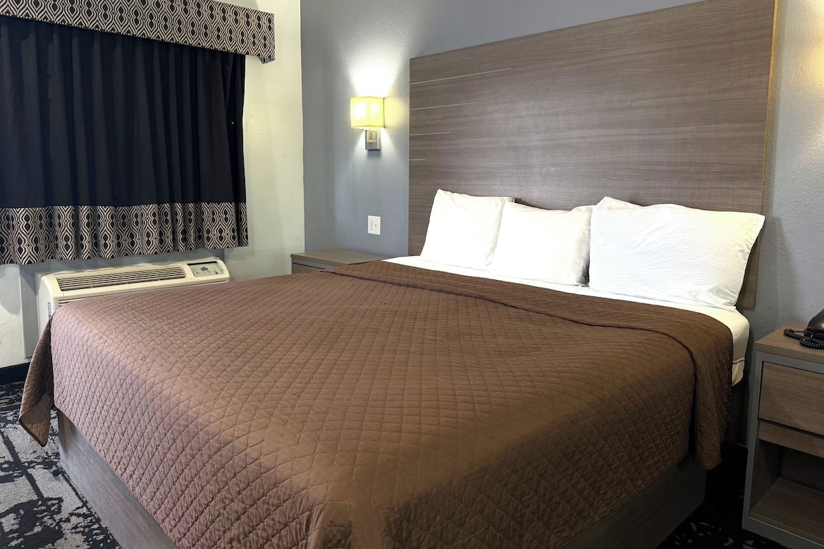 A hotel room with a large bed, a bedside table, a lamp, and a window with curtains.