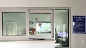 A hotel reception area with a glass door, a clock, and a welcome sign listing hotel policies.