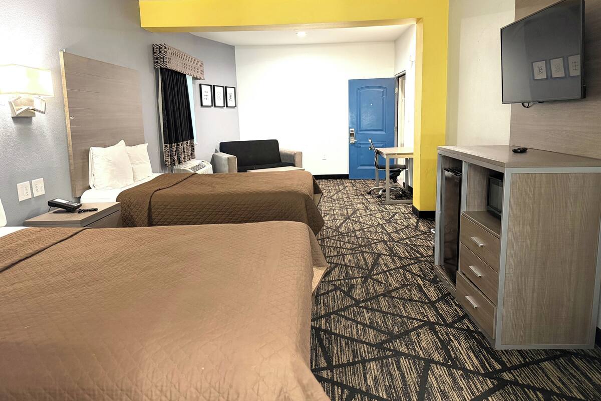 A hotel room with two beds, a desk, a chair, a TV, and a wardrobe.