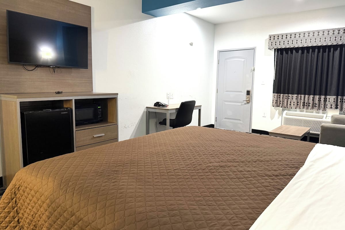 A hotel room with a large bed, a desk, a television mounted on the wall, a microwave, and a door with a patterned curtain.