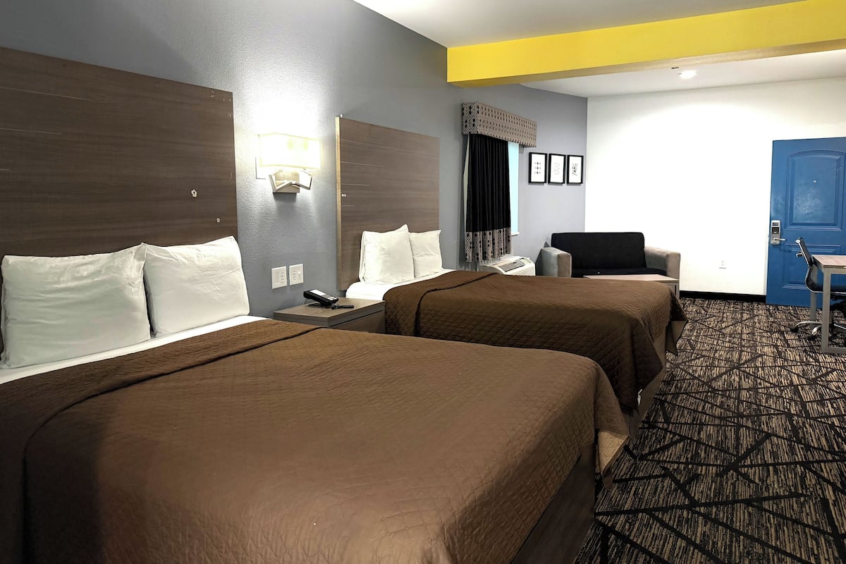 A hotel room with two beds, a desk, a chair, and a blue door.