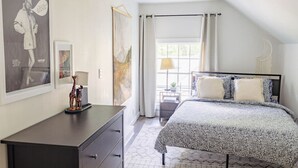 Une chambre à coucher avec un lit, une commode, une table de chevet, une lampe et des œuvres d’art accrochées aux murs.