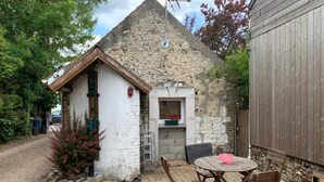 Ein rustikales Steinhaus mit einem kleinen Anbau, einer Ziegelterrasse und einem runden Tisch mit Stühlen.