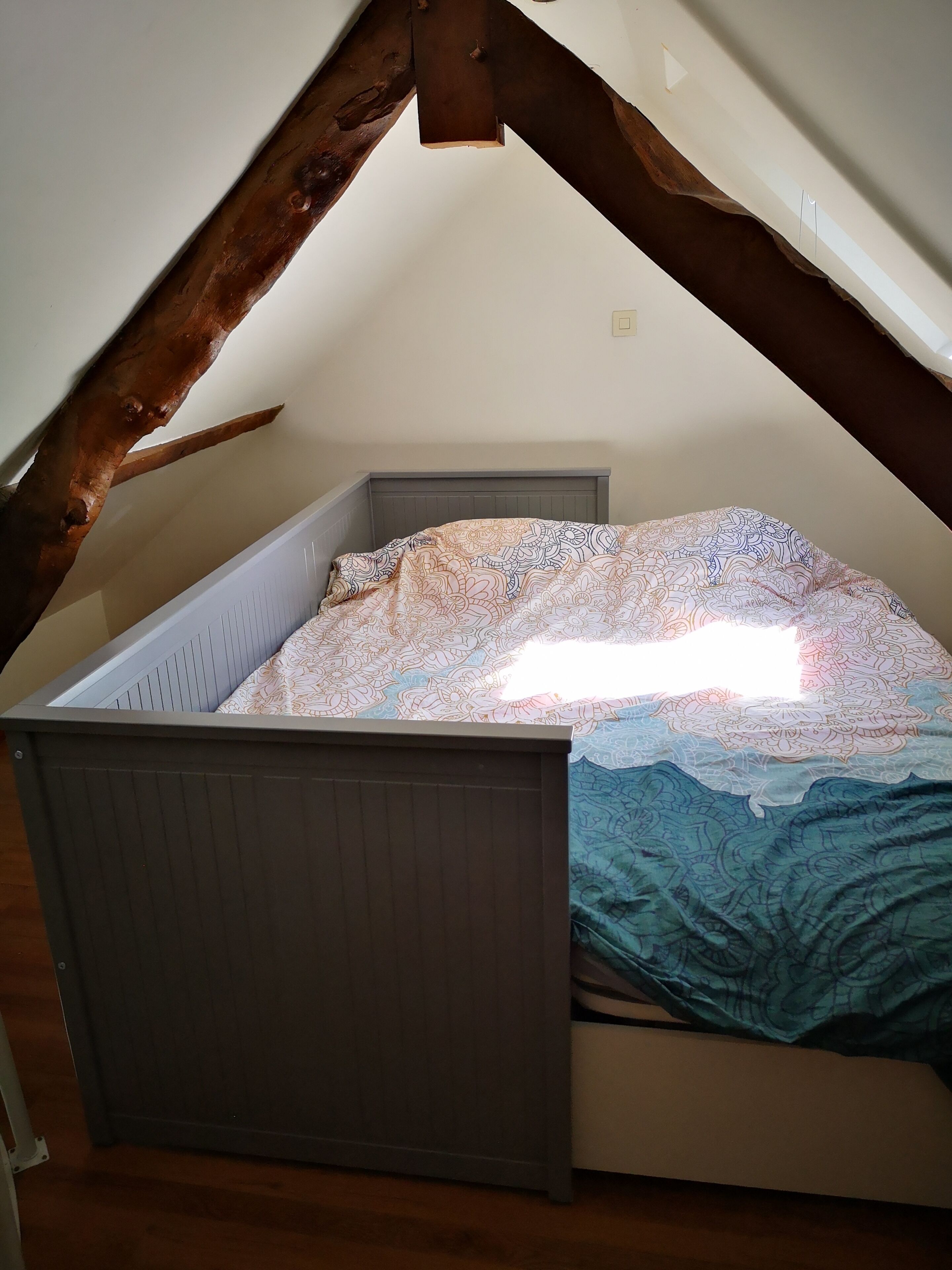 A small, slanted room with a bed, wooden beams, and a window.