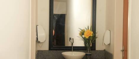 Un baño con un lavamanos blanco, un espejo y un florero con flores amarillas.