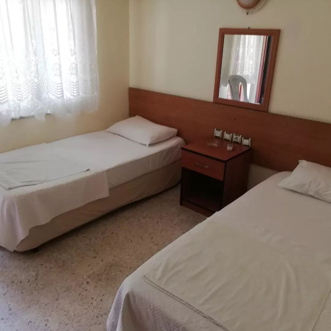 Una stanza con due letti singoli, un comodino in legno con un telefono e uno specchio a parete.