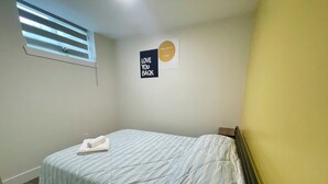 Una camera da letto con un letto, una finestra con persiane, una targa appesa al muro e una piccola pianta.