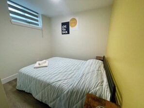 Un dormitorio con cama, ventana con persianas, un cartel en la pared y una planta pequeña.