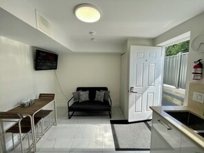 A compact room with a bed, a desk with chairs, a television, and a door leading outside.