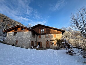 A stone house with wooden shutters and a sloped roof, surrounded by snow.