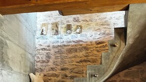 Un escalier en colimaçon, avec un mur de pierre en arrière-plan, un plancher en bois et une statue blanche sur la gauche.