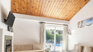 Une pièce avec un plafond en bois, un canapé, un téléviseur et une vue sur une piscine.