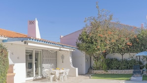 Une maison avec un patio, une table à manger avec des chaises et un arbre aux fleurs oranges.