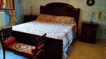Camera da letto con un letto, una sedia di legno, un comodino, una croce appesa al muro e quadri incorniciati.