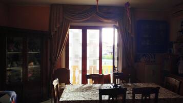 A dining area with a table set for four, a cabinet with glass doors, and a view through a large window with curtains.