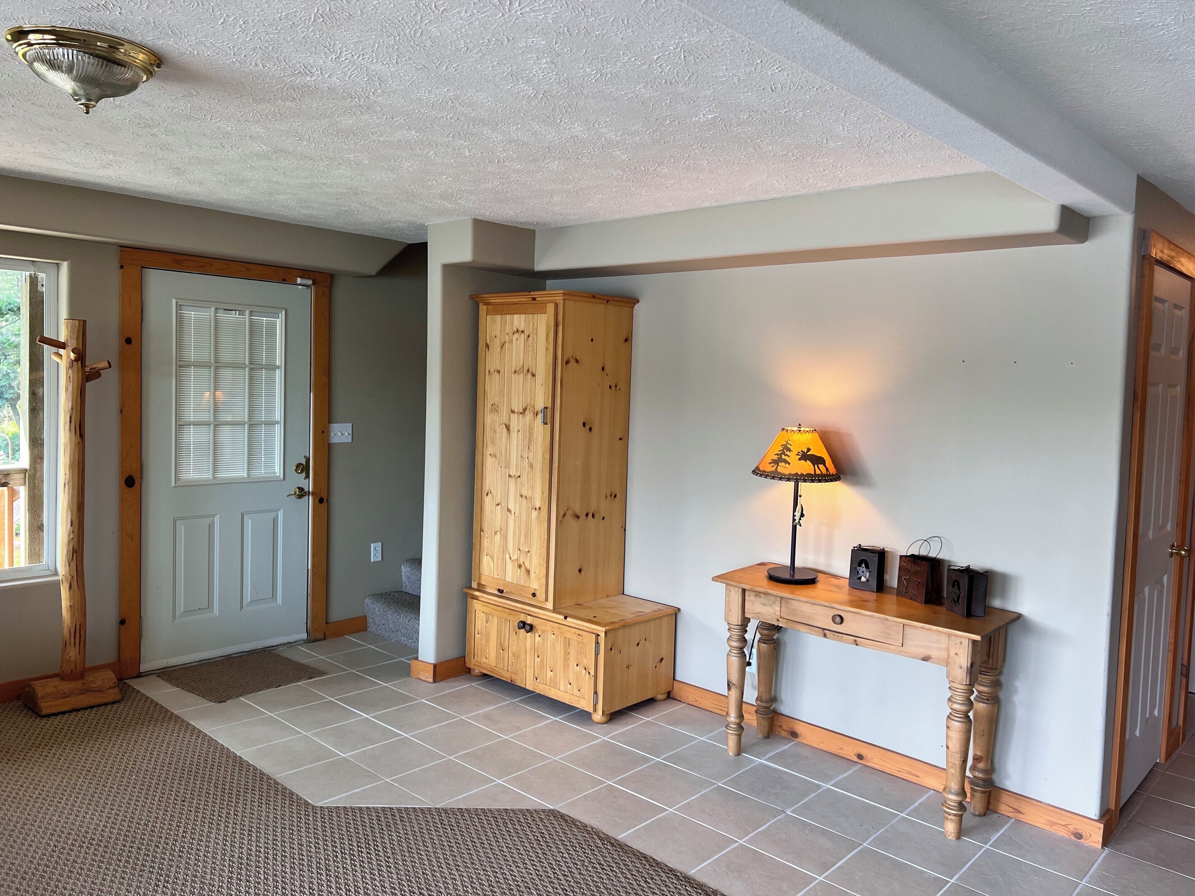 A hallway with a wooden cabinet, a table with a lamp, and a door with blinds.