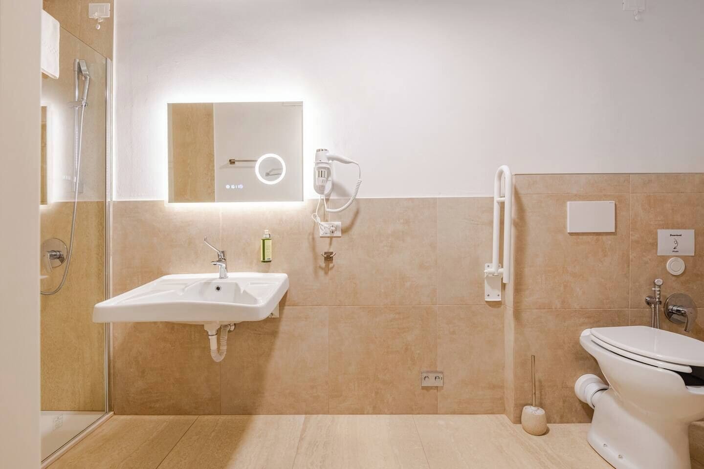 Un baño moderno con lavamanos, espejo, ducha de mano y retrete.