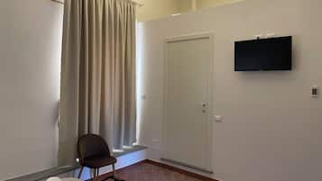Una camera d'albergo con un letto, una sedia, una televisione, una porta e una finestra con tende.
