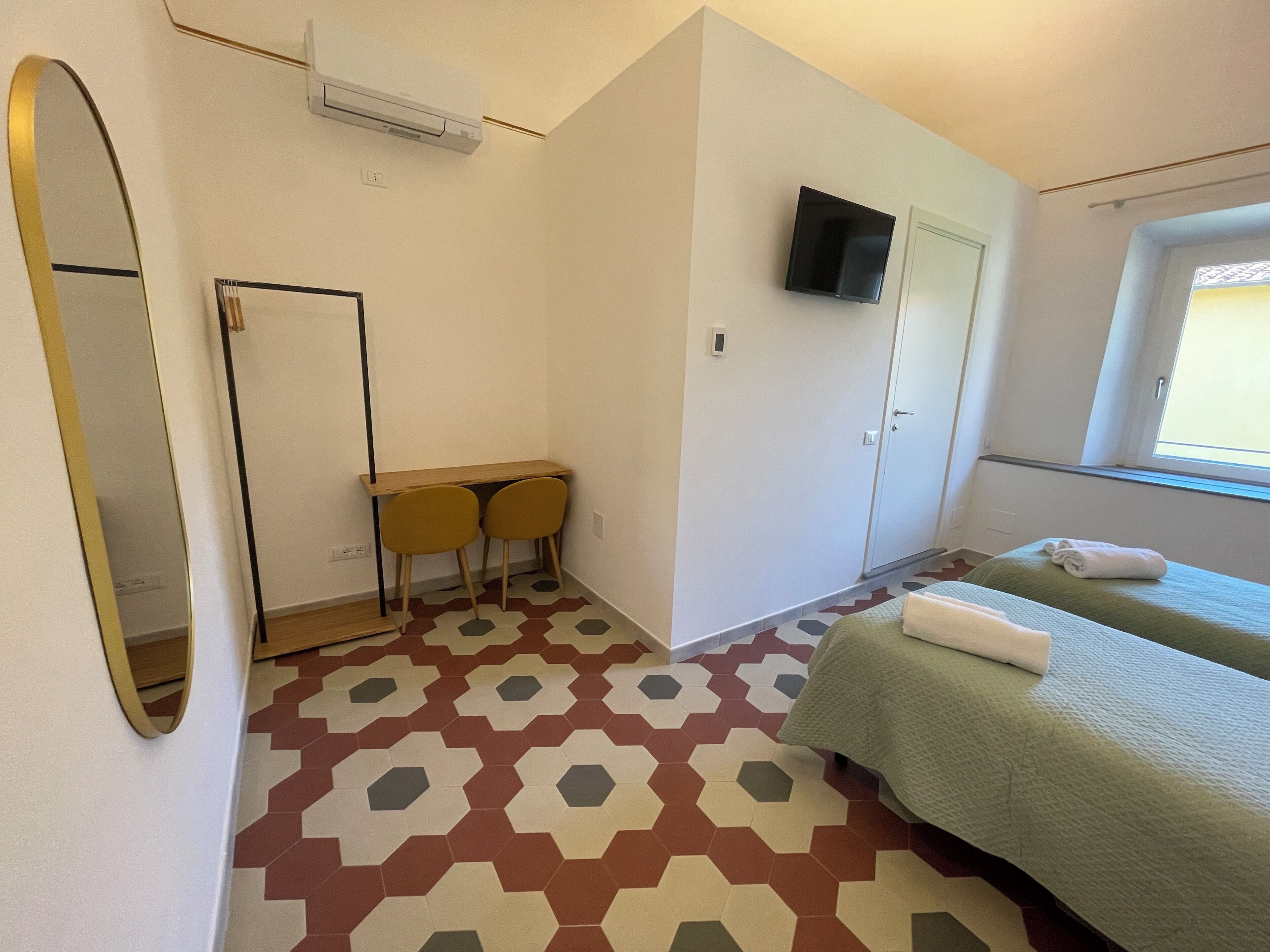 Una habitación con una cama, un escritorio con dos sillas, un televisor en la pared y un ventanal con vistas.