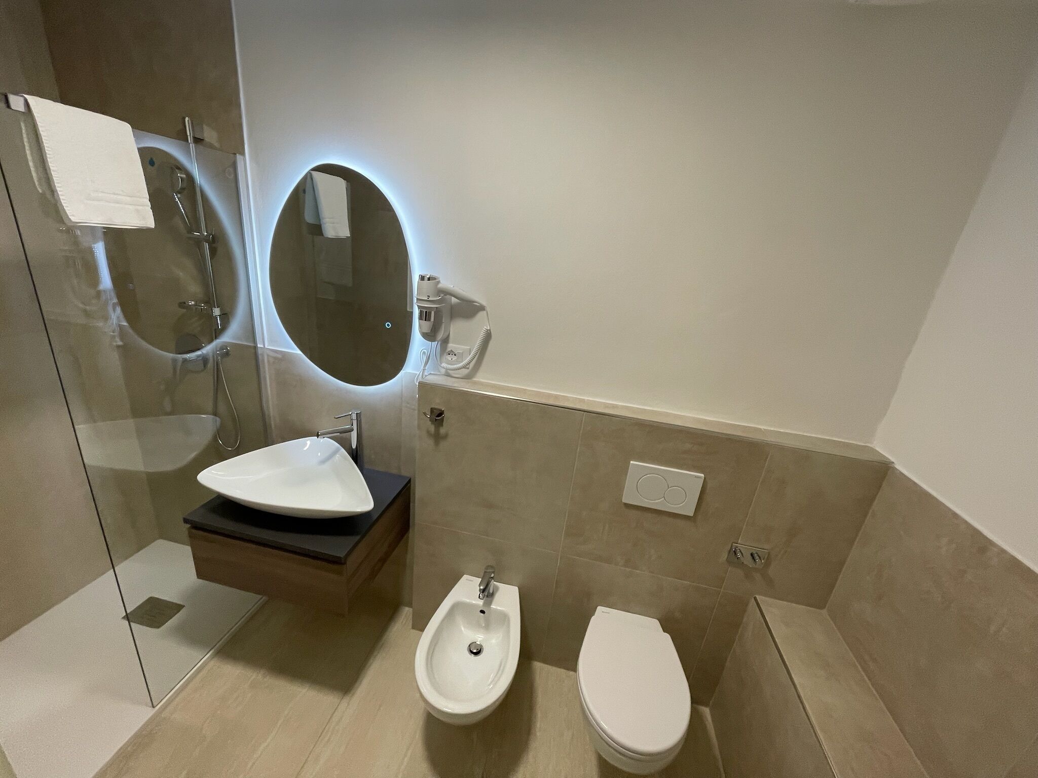 A modern bathroom with a glass-enclosed shower, a white sink, a bidet, and a toilet.