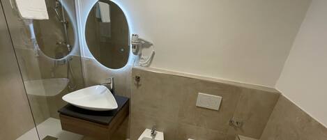 A modern bathroom with a glass-enclosed shower, a white sink, a bidet, and a toilet.