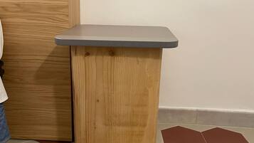 Una pequeña mesa de madera con tapa gris, colocada junto a una pared con puerta de madera y suelo de baldosas con patrones hexagonales.