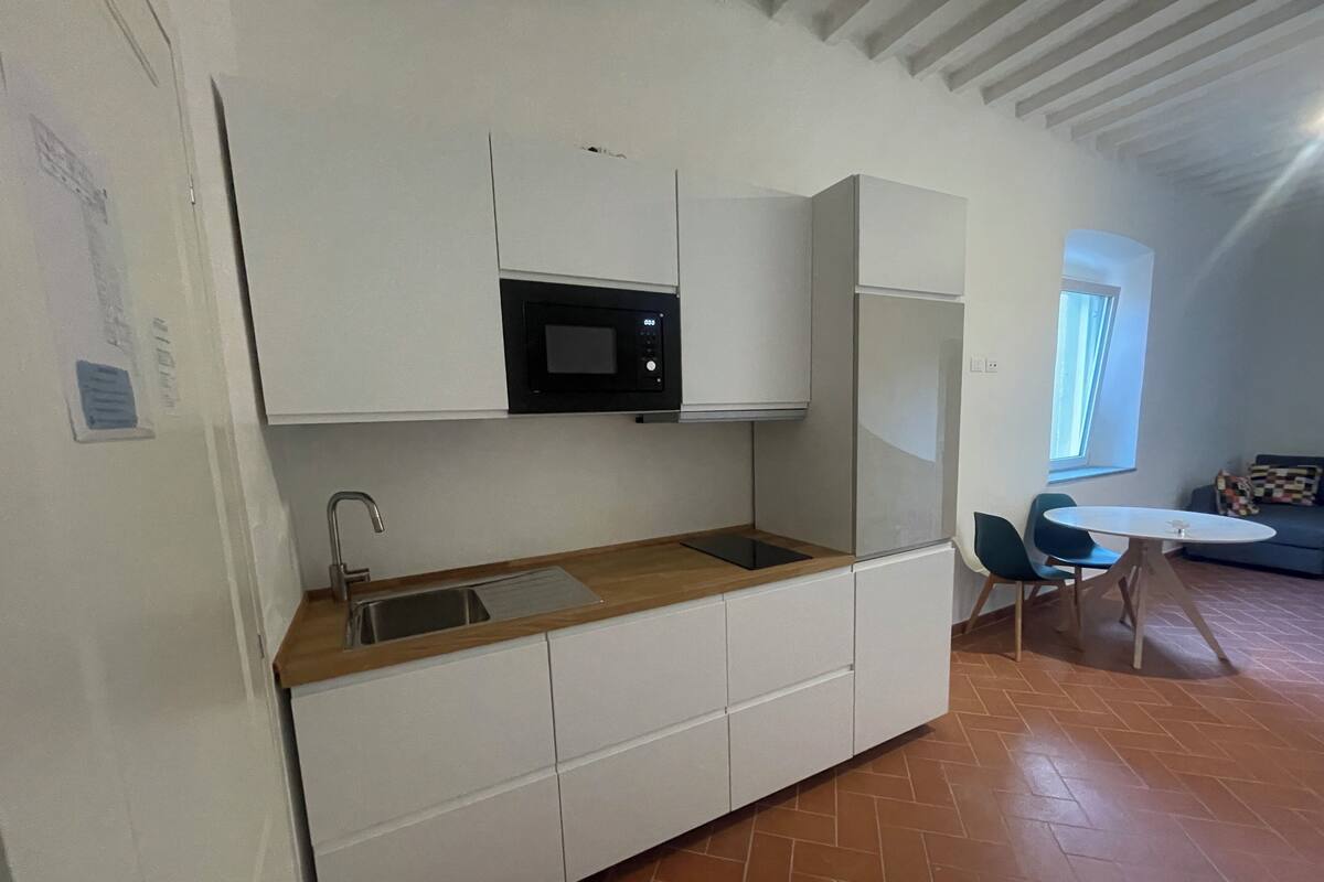 A compact kitchen with white cabinets, a microwave, a sink, and a wooden countertop. There is a dining area with a round table and chairs.