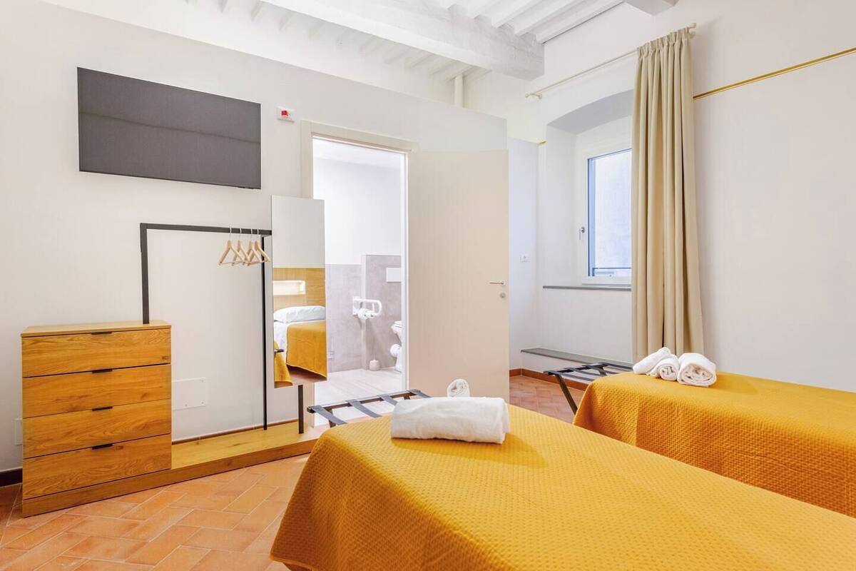 A hotel room with two beds, a wooden dresser, a TV mounted on the wall, and a window with curtains.