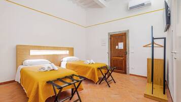 Habitación de hotel con dos camas, un armario de madera, un perchero y piso de baldosas.