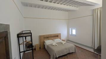 Un dormitorio con cama, una ventana pequeña, cabecera de madera, un perchero y suelo de ladrillo.