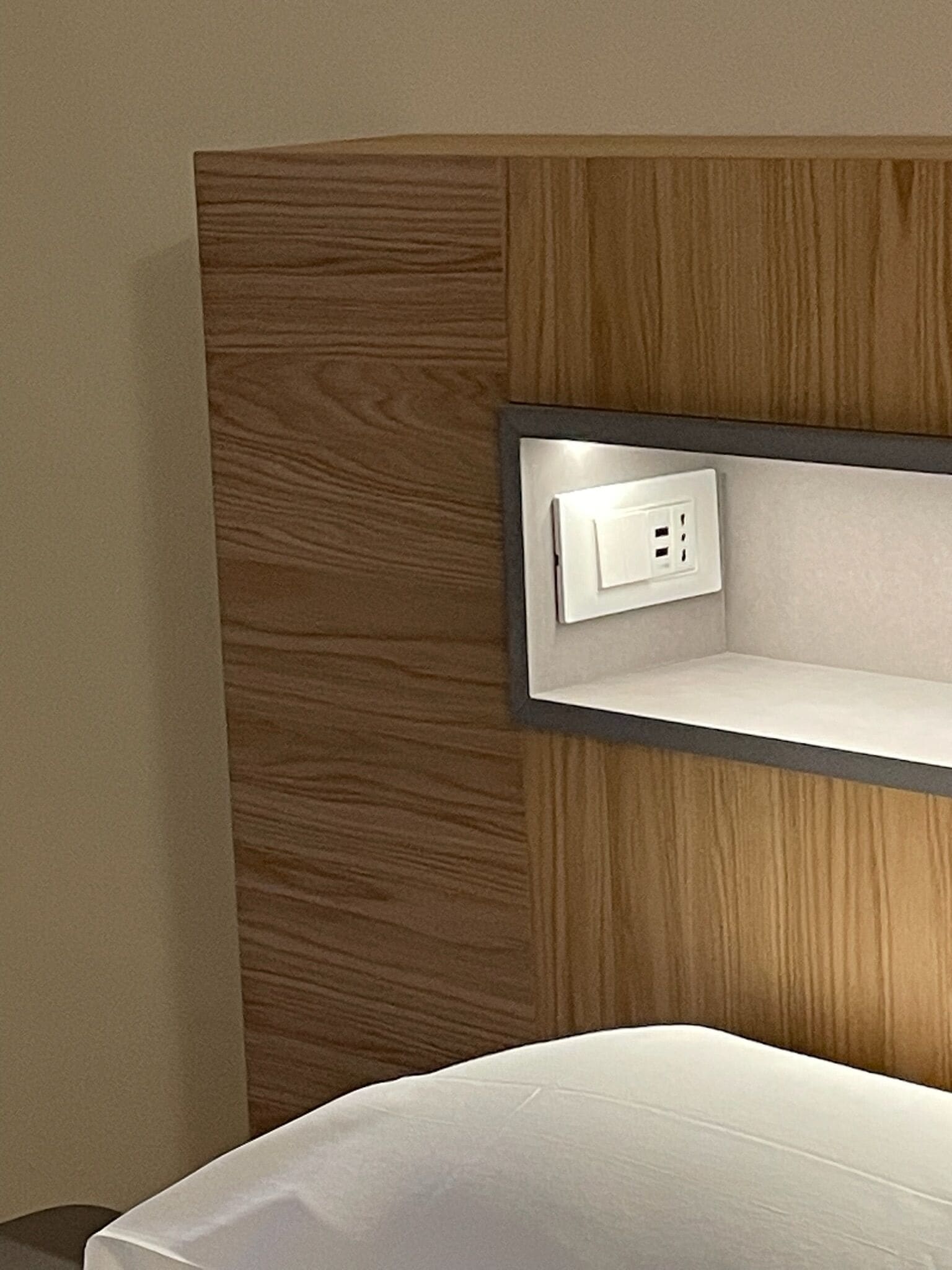 Une chambre d’hôtel avec un mur recouvert de panneaux de bois, une table de chevet blanche et une prise électrique intégrée.