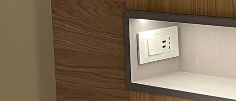 A hotel room with a wooden panel wall, a white bedside table, and a built-in electrical outlet.