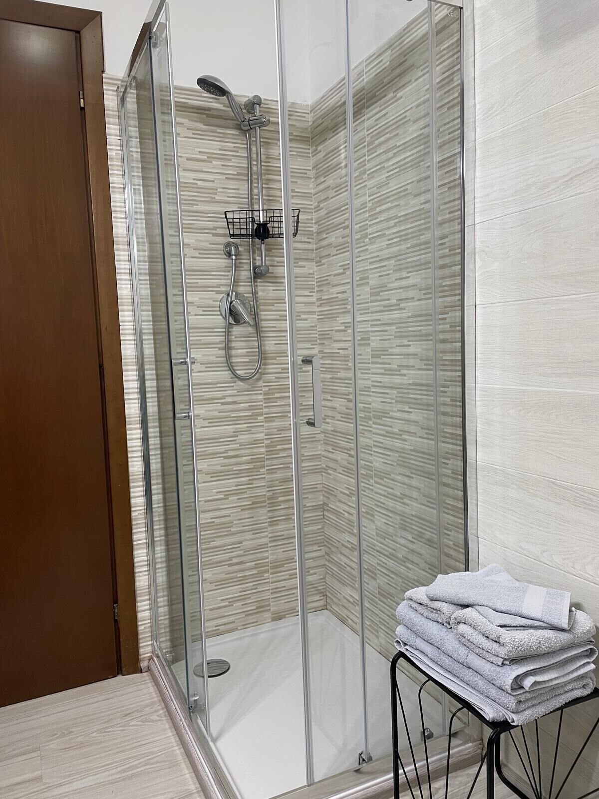 Ducha con cerramiento de vidrio, cabezal de ducha de mano y grifo empotrado.