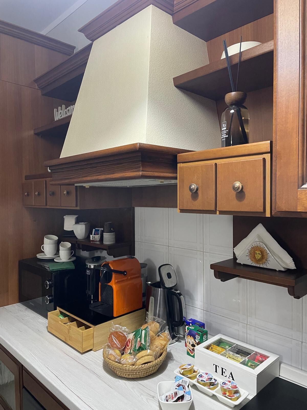 Una cocina con armarios de madera, cafetera, hervidor, una cesta de pan y una selección de tés.